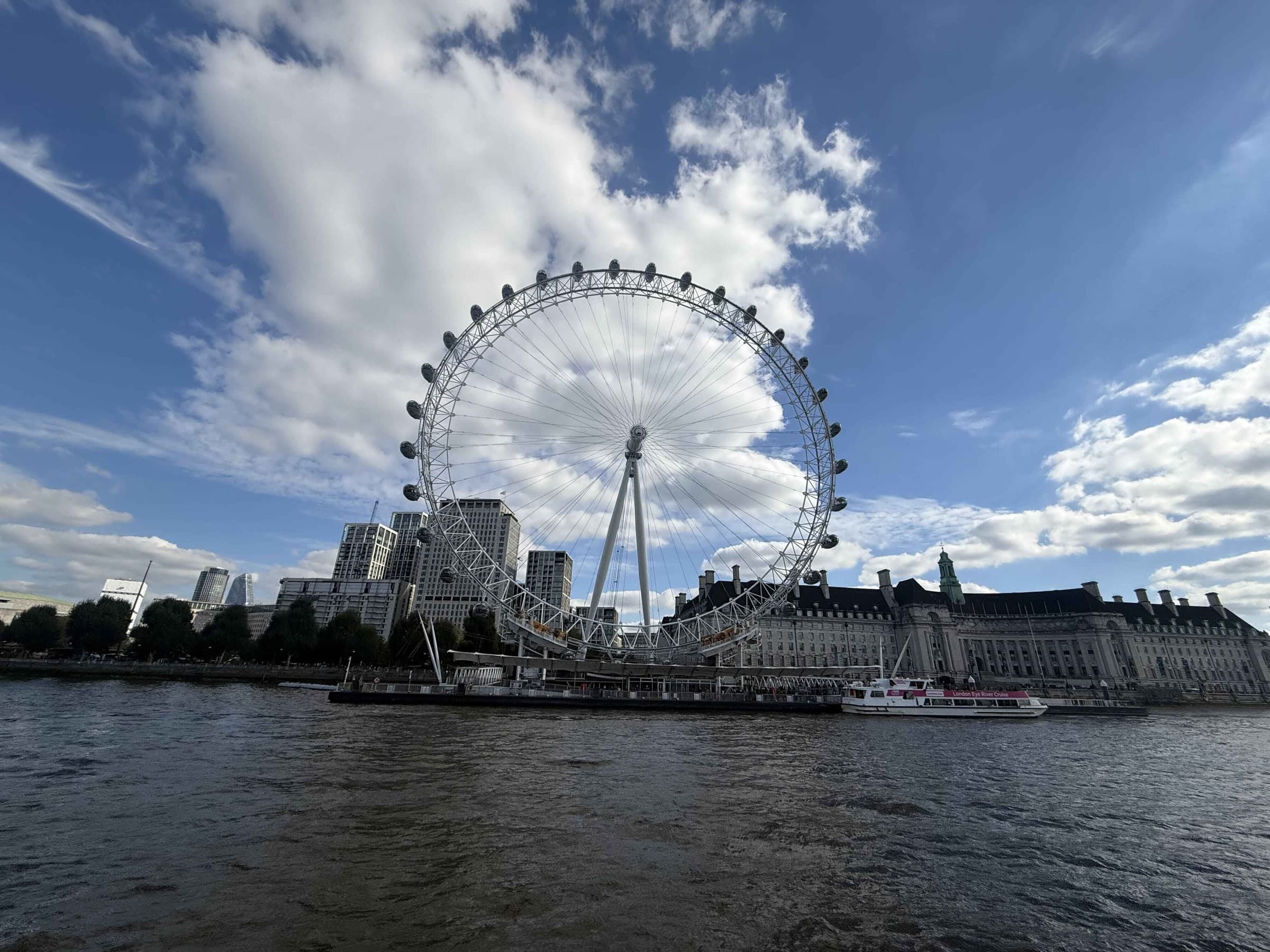 The London Eye across the Thames under a bright, cloudy sky