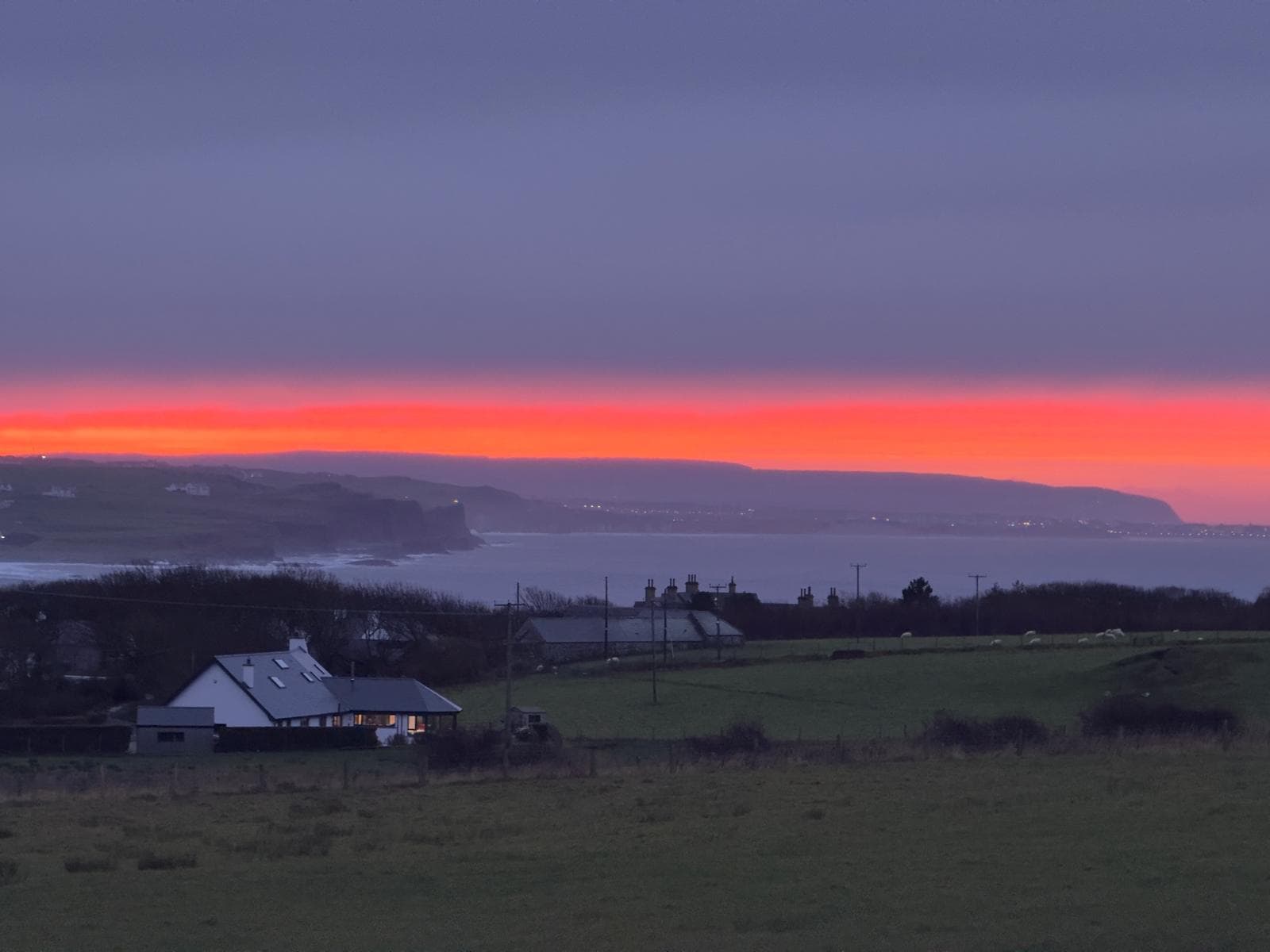 A red band of sunset over the coast and a cottage at dusk