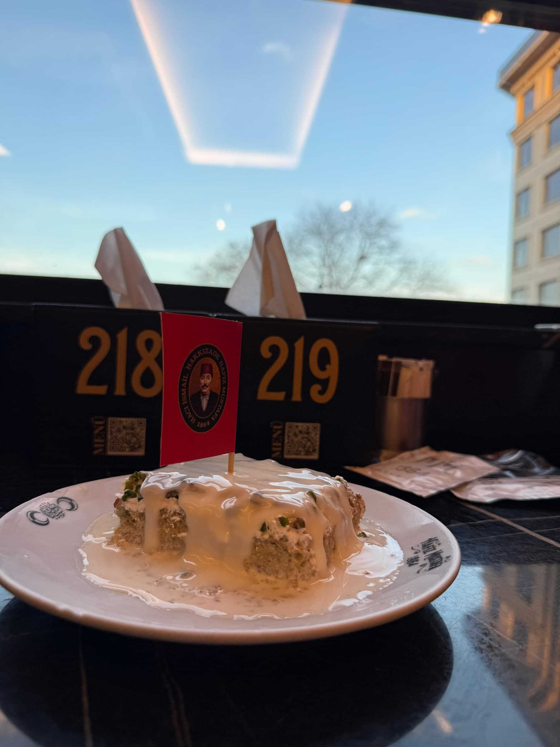 A milk-soaked pistachio dessert on a plate at a café table